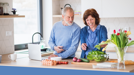 A senior couple in a kitchen preparing a meal.