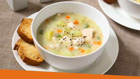 A soup sitting in a bowl on a plate with pieces of the bread on the plate.