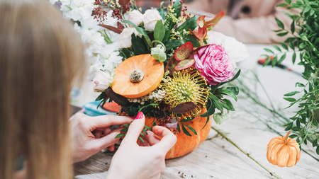 A person creating a floral arrangement inside a pumpkin.