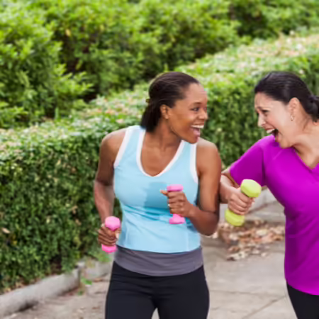two women, one Hispanic, the other African American walking on a sidewalk carrying hand weights in the spring