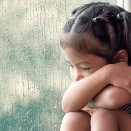 Sad preschooler sitting next to a window on a rainy day