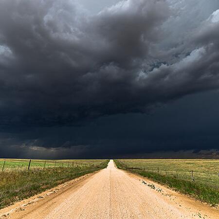 dirt road leading toward a dark cloudy stormy sky
