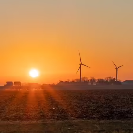 A sunrise over a farm field and wind turbines