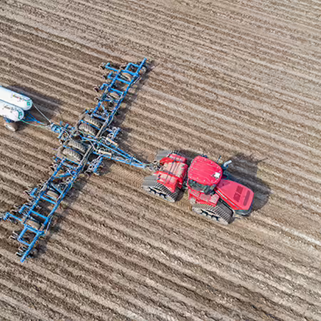 A tractor pulling anhydrous tanks across a field.