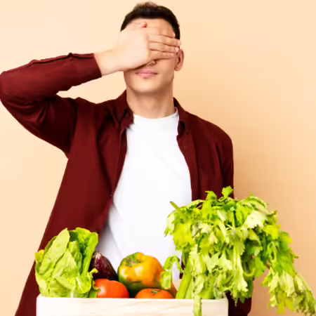 Person standing by a crate of vegetables with their hands over their eyes