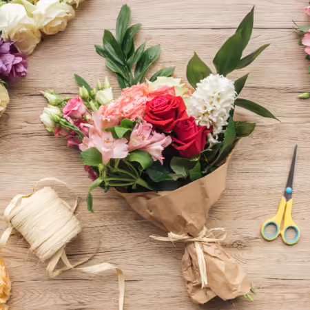 Mixed bouquet of pink and white flowers wrapped in paper on a wooden table surrounded by other flowers ready for a bouquet