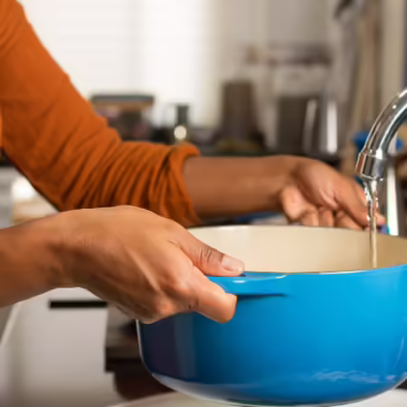 Women filling a blue pot with water at kitchen sink