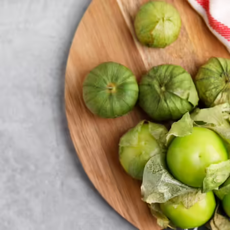 Tomatillos on a round wood board with a decorative red and white towel