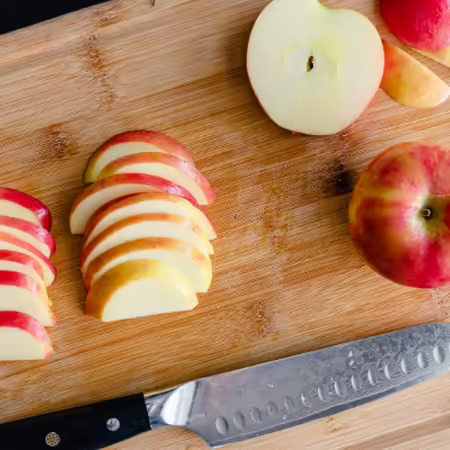 Sliced apples and apple halves on wood cutting board with knife