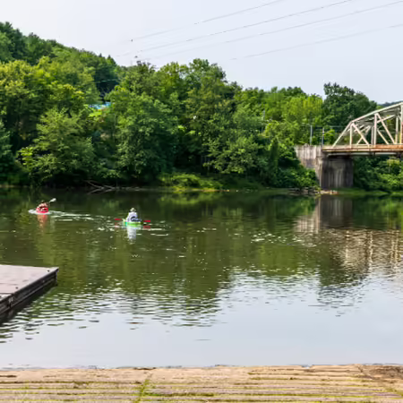 two kayakers paddle away from put-in on a placid river near bridge