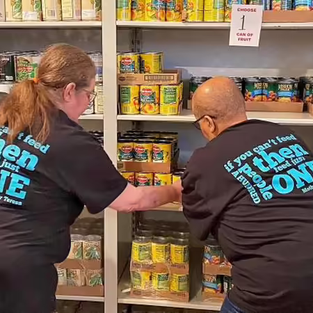 two ladies with their backs to the camera stocking shelves at a food pantry