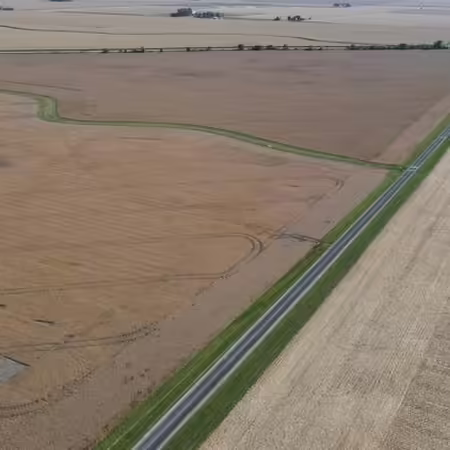 Aerial view of various farm fields with road running diagonally inbetween.