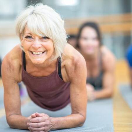 senior woman in purple tank top holds a plank position in a yoga class