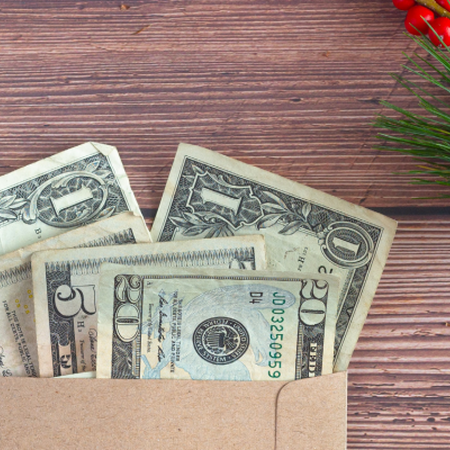 One, five, and twenty dollar bills in an envelope on a table decorated with greenery and red berries.