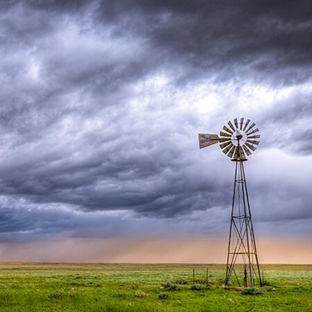 Stormy clouds moving across a windmill in a Midwest pasture. 