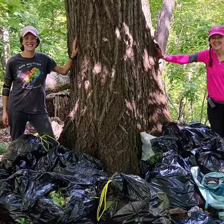 two ladies standing in the woods with five garbage bags full of garlic mustard
