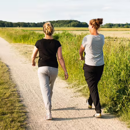 Two people walk on a dirt path through a prairie landscape