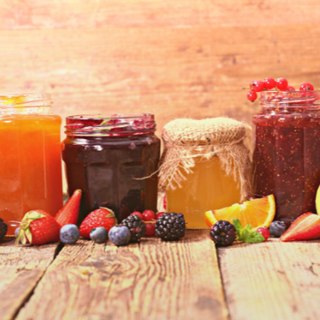 Image of a variety of fruit jams in jars with a variety of fruit and berries scattered in front of the jars