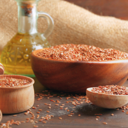 Flaxseed oil next to wooden spoons and bowls filled with flaxseed