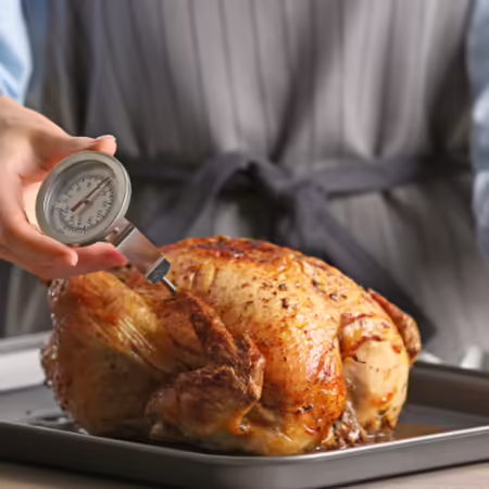 Checking the temperature of chicken with a thermometer placed in the chicken breast.