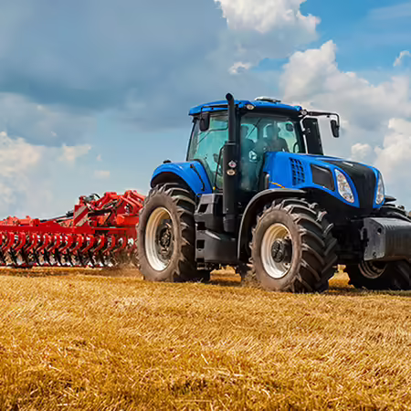 A blue tractor with a red implement in a field. 