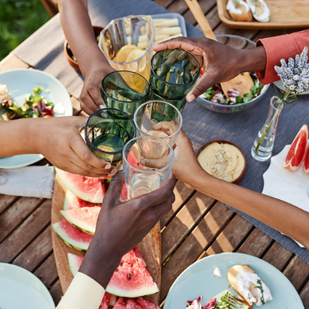 Hands on an African American family raising glasses in a toast over a table of summer foods