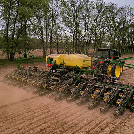 A green tractor pulling a planter across a field. 