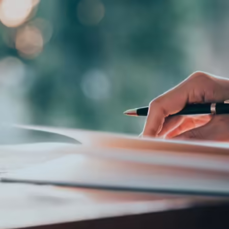 hand holding pen and lightly holding down pages of book