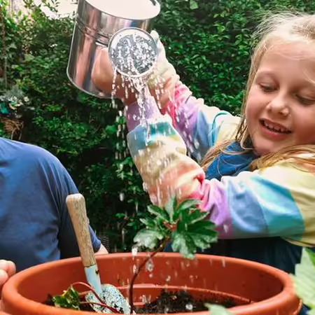 A child watering a plant with an adult watching 