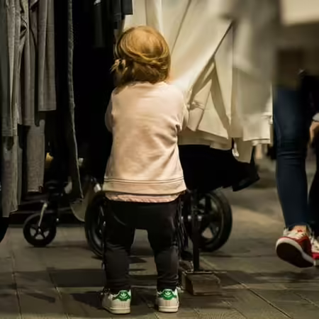 child standing near clothing in store