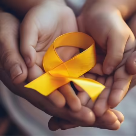 A parent hold their child's hands holding a yellow ribbon to represent childhood obesity awareness.