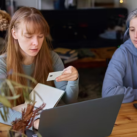 Two woman, one woman looking at credit card and computer