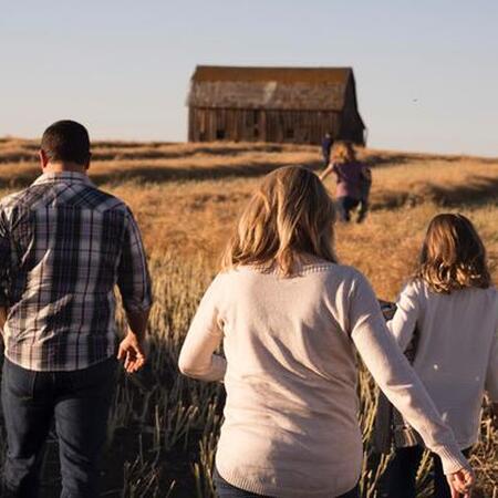 family running through a field toward an old barn