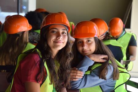 two girls in orange hard hats and yellow vests