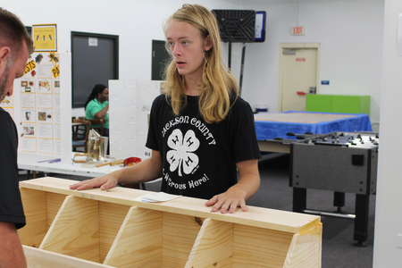 A teen shows his woodworking project to a 4-H judge.