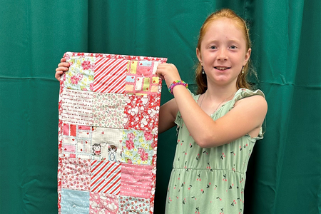 Girl in green dress holding up a quilt