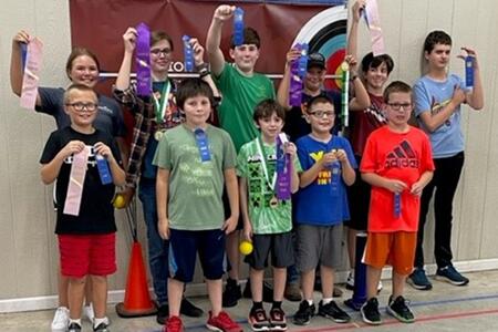 11 kids standing in 2 rows and holding up award ribbons