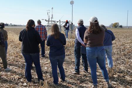 Group of people on a farm tour standing listening to a speaker 