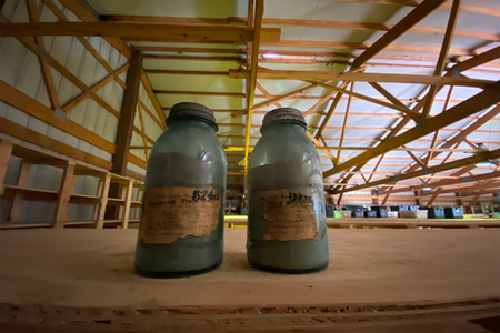 Two soil samples collected in jars sitting on a shelf inside a shed. 