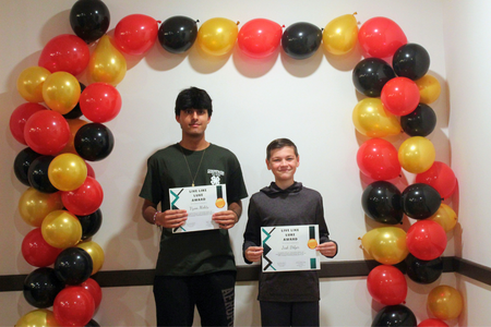 Two boys stand with certificates that say they won the Live Like Luke Award in front of a balloon arch.