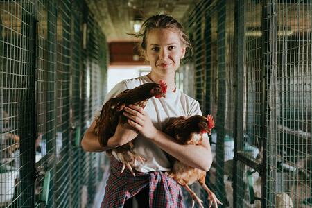 Person holding two chickens and smiling at the camera in a chicken coop.