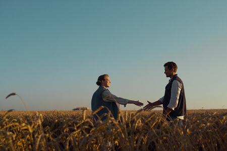Two people talking, about to shake hands in a wheat field.