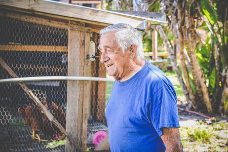 A farmer wearing a hearing aid while doing outdoor chores at a chicken coop.