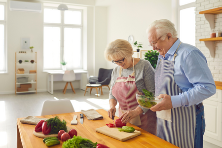 An older couple chopping vegetables in a brightly lit kitchen.