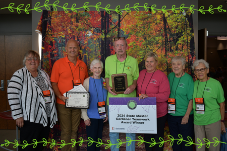 Image of a group of people holding a sign and award with plant vine graphics.