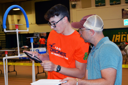 A 4-Her looking at a tablet while flying his drone as an instructor assists.