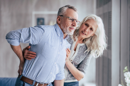 An elderly woman assists an old man in pain