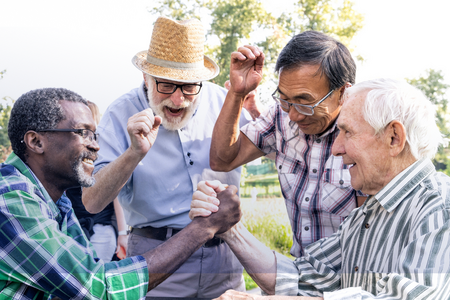 two elderly men arm wrestling while two more cheer them on