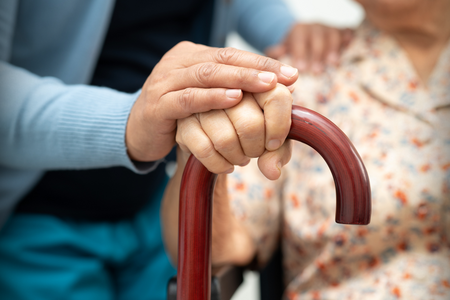 an elderly hand and a caregiver hand resting on a wooden cane