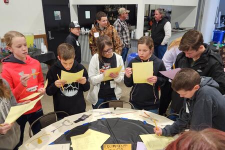 a group of kids standing around a table writing on paper